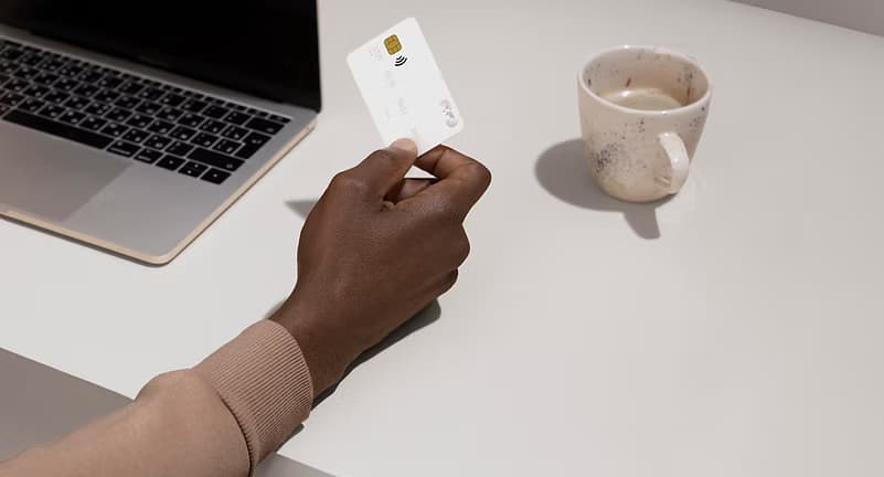 A person holding a payment card beside a laptop